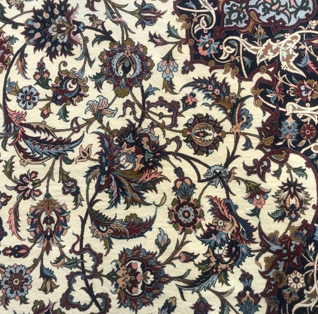 Detail of an Isfahan carpet designed by Mirza Agha Emami and woven by Ahmad Zojaji, showing dense Shah Abbasi floral scrollwork on a cream field meeting a navy border