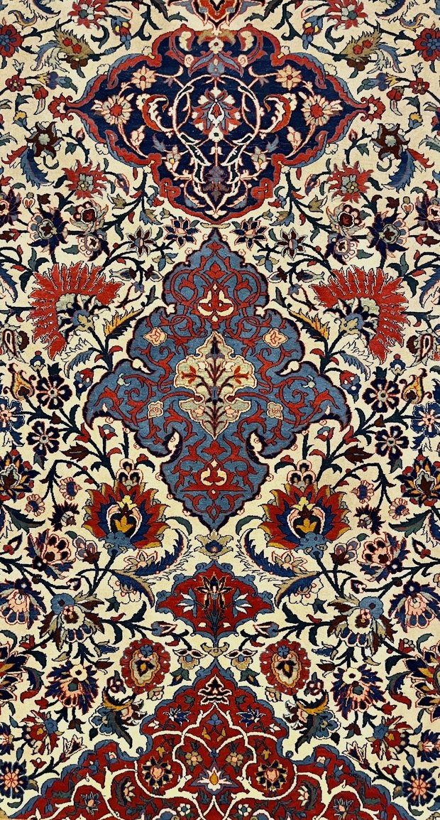 Detail of an Isfahan carpet by Haj Mehdi Khan Safdarzadeh Haghighi, a navy top medallion and central blue cartouche on a dense cream Shah Abbasi floral field.