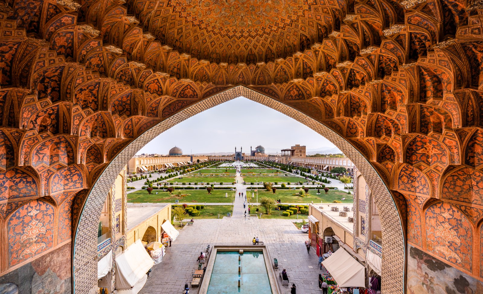 The Naqsh-e Jahan square in Isfahan framed by the honeycomb muqarnas vault of the Gheisariye, the entrance to the royal bazaar, with the Shah Mosque dome visible at the far end of the maidan