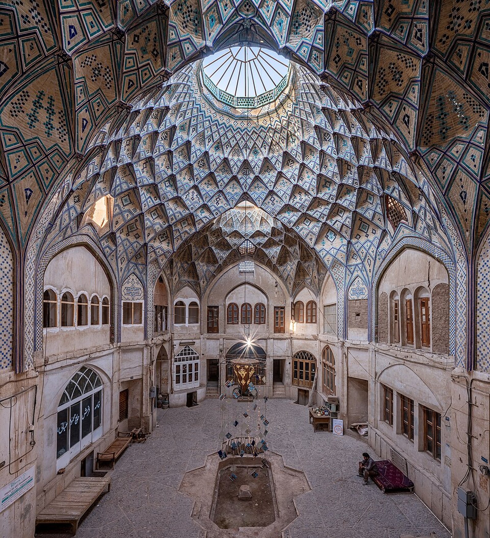The tiled muqarnas dome of the Bakhshi caravanserai in the Kashan bazaar, its vaulted brick hall lit from a central oculus