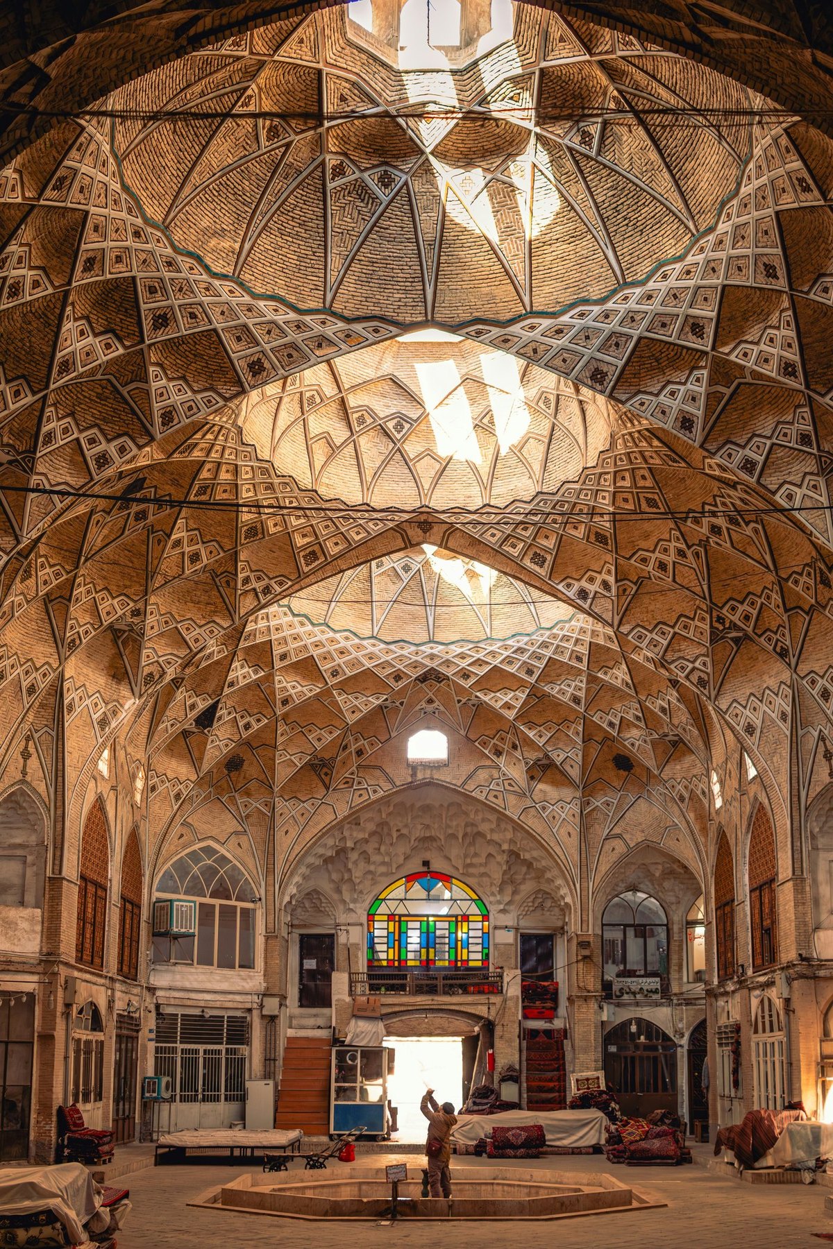 The vaulted brick dome of the Timcheh, the historic carpet caravanserai in the Qom bazaar, lit by a central skylight, with carpet shops below