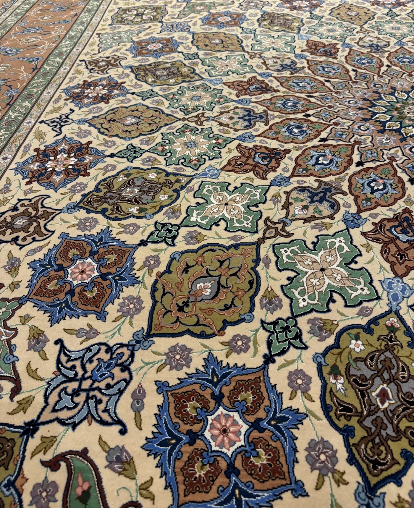 The field seen at an angle, its lattice of star-medallions and cartouches in green, blue, and soft rose running across the cream ground to the border.