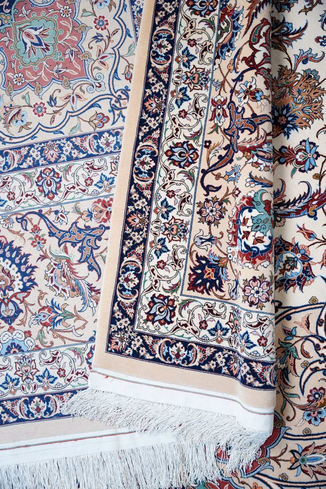 The border system folded back over the field: navy guard bands, the camel outer border, the white silk fringe and kilim end, a rose corner medallion showing above.