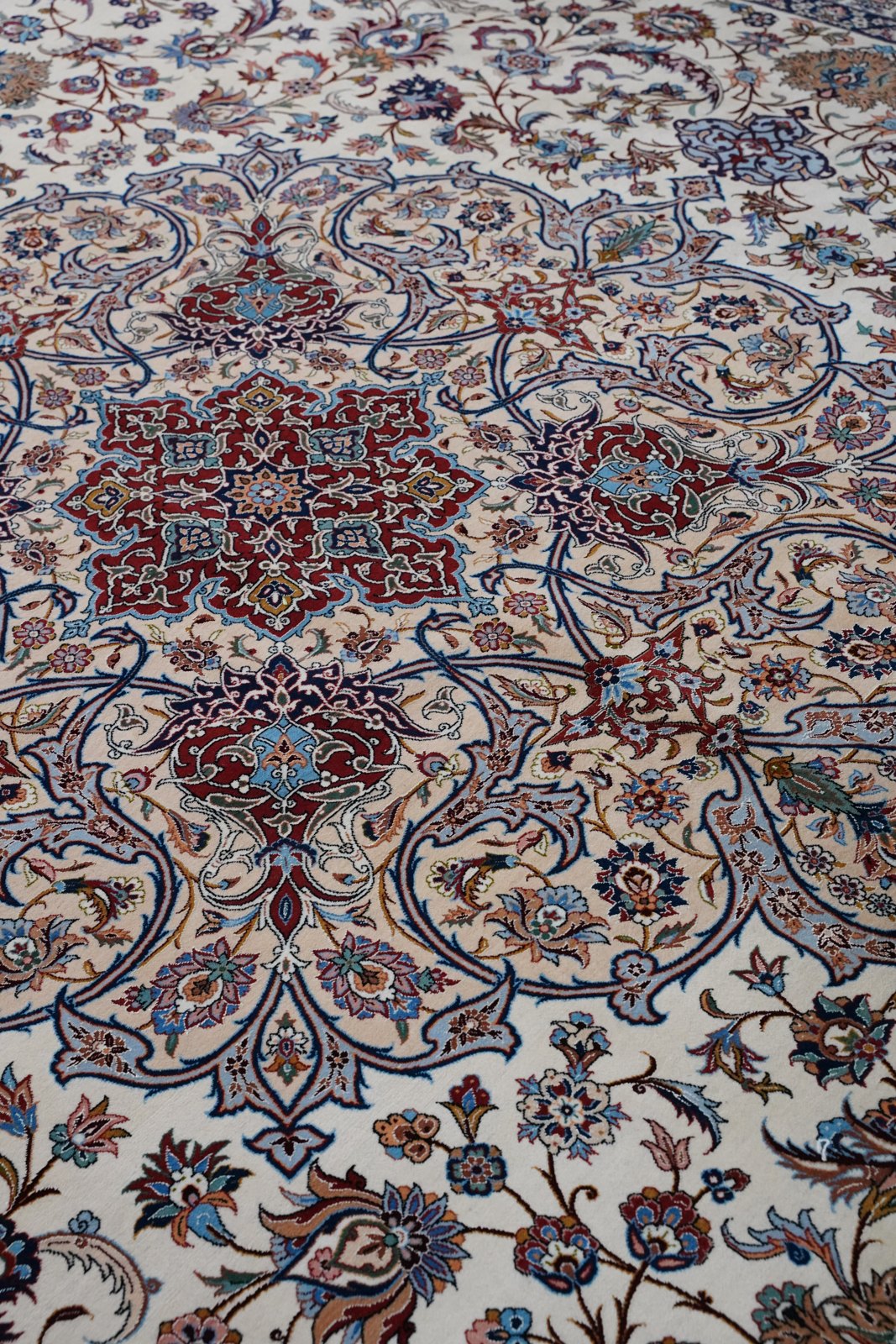 The pile in soft folds, madder and navy drawing over the ivory ground, the silk catching light along each crest.