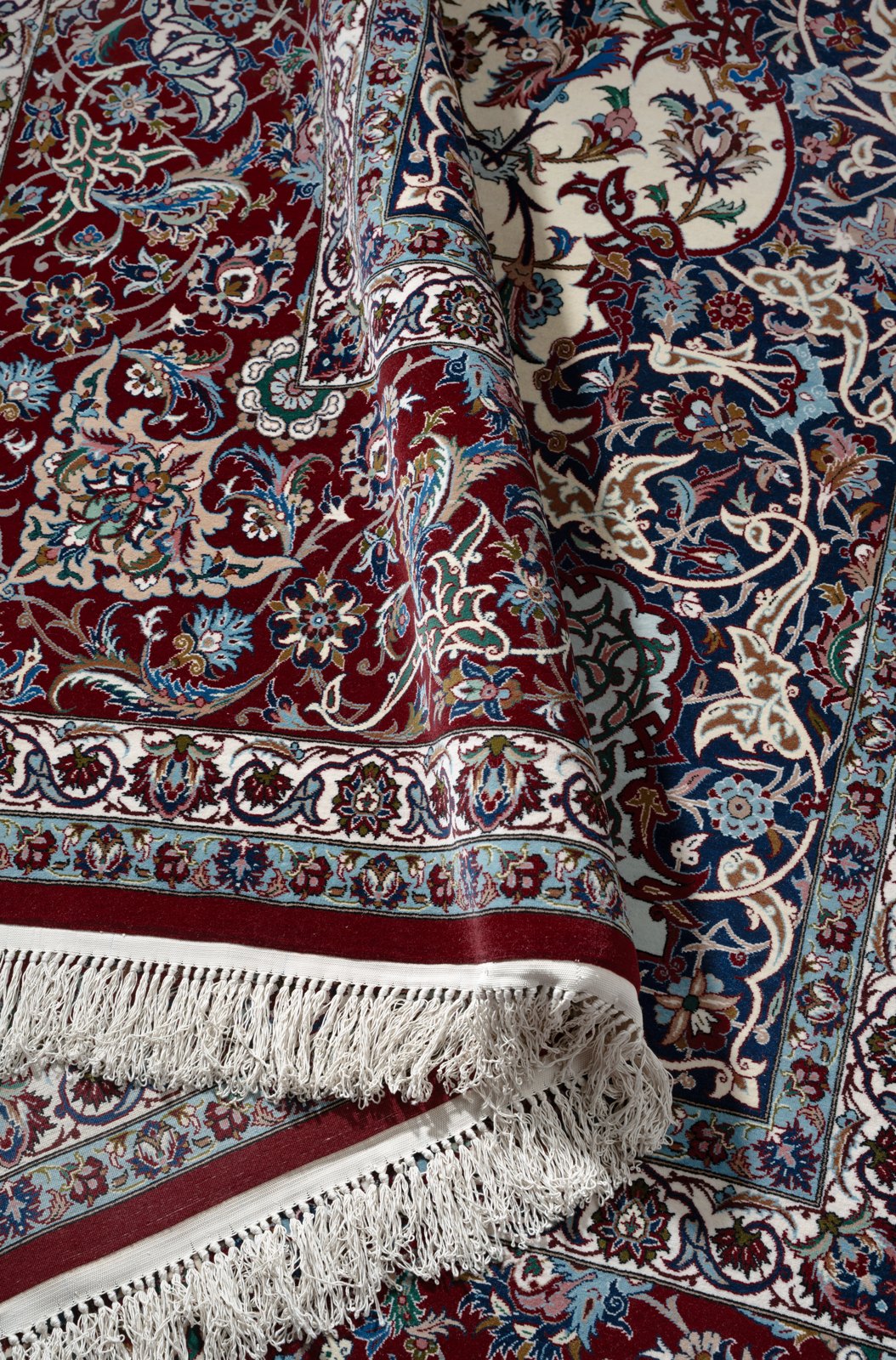 The carpet folded over itself, the white silk fringe and kilim end in the foreground against the border.