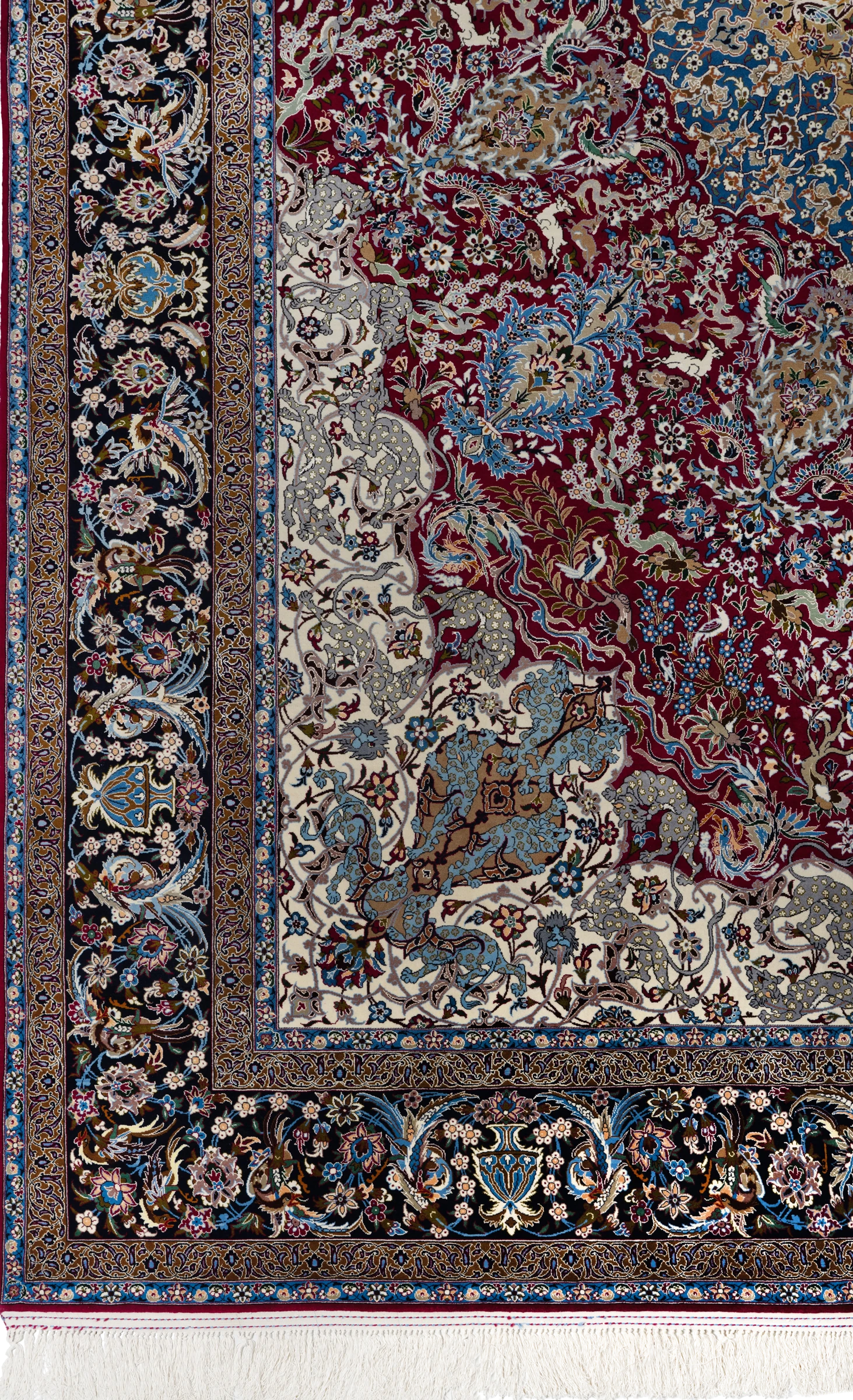 The corner of the carpet, full bleed: the navy-and-camel border system turning the angle, the ivory spandrel&rsquo;s grey and blue beasts, the madder field&rsquo;s birds and blossoms, and the white silk fringe at the foot.