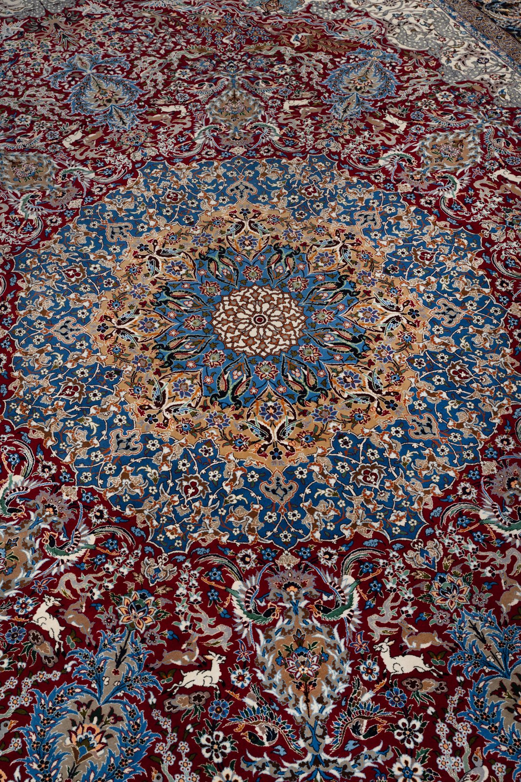 The sunburst medallion at an angle: an ivory core opening through gold and blue rings onto the madder field, white deer leaping below.